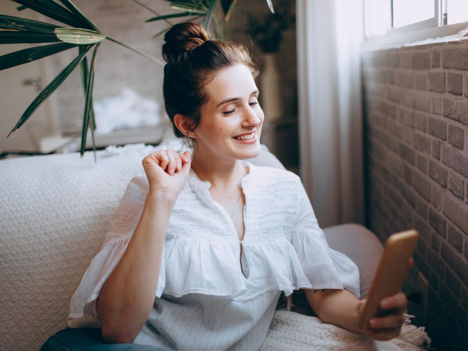 A patient by her window, smiling as she reads on her phone