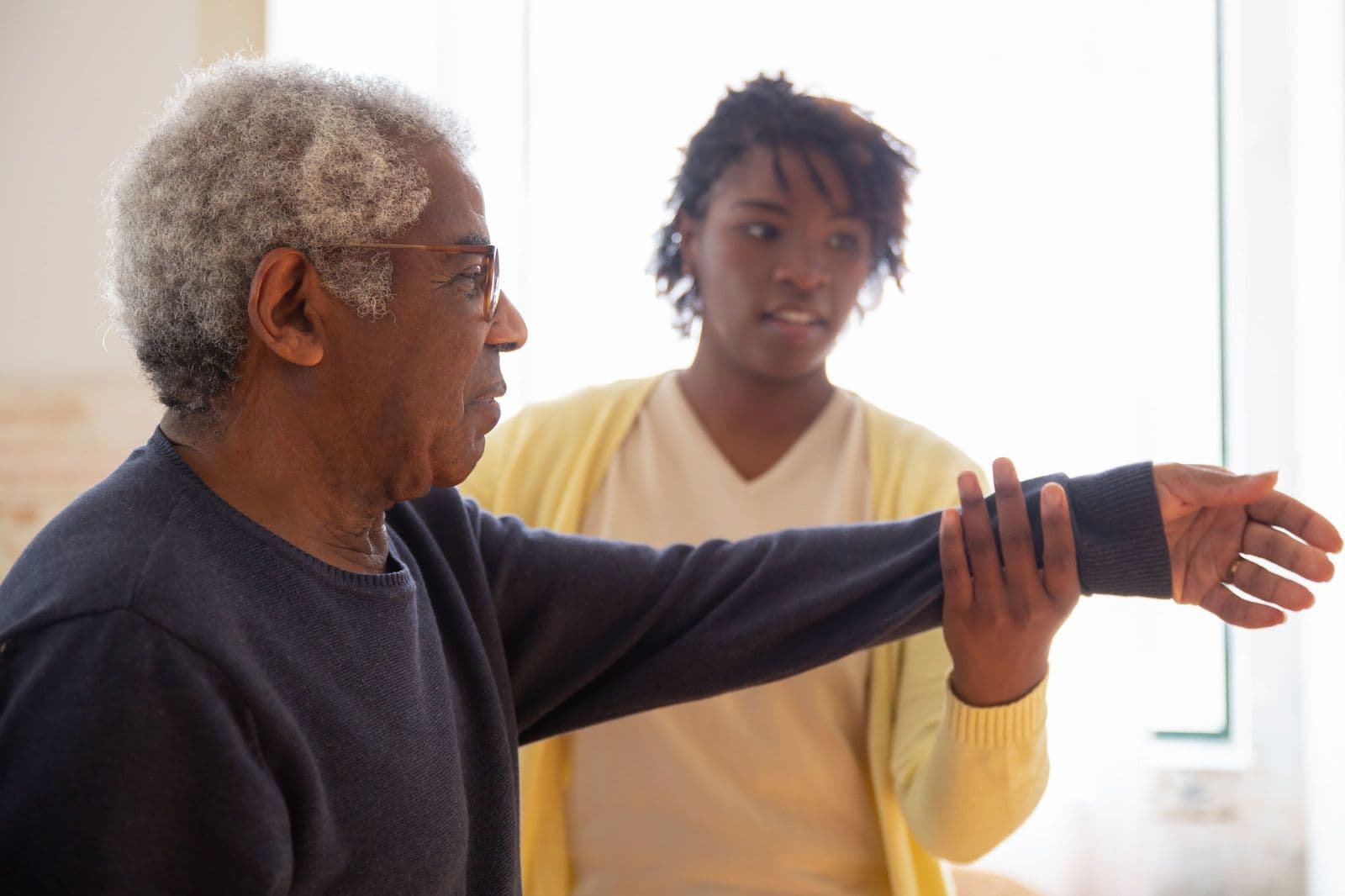 A physiotherapist guiding an older patient through an arm exercise in their living room