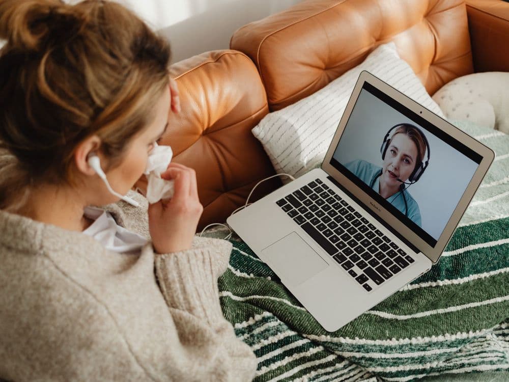 A patient on her sofa in a video session, her physiotherapist live on the laptop screen